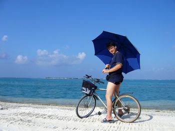 Portrait of man holding umbrella while riding bicycle at beach