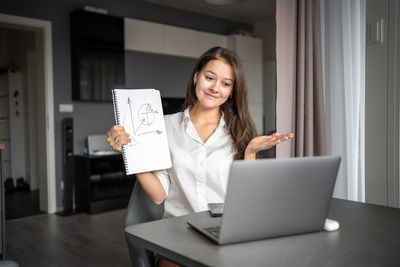 Portrait of young woman using laptop while sitting on table