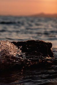 Rock on sea shore against sky during sunset