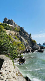 Scenic view of rocks by sea against clear sky