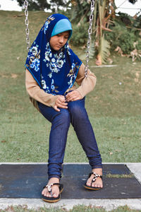 Full length of girl wearing hijab sitting on swing in playground