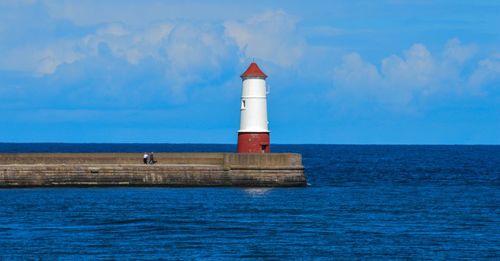 Lighthouse on calm sea against blue sky