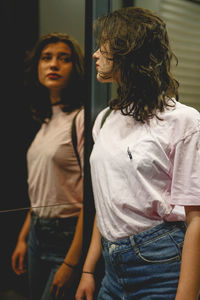 Woman with reflection in mirror leaning on wall