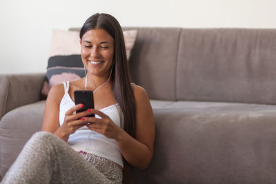 Smiling woman using mobile phone while sitting by sofa at home