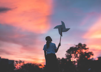 Young woman holding pinwheel toy while standing against sky during sunset