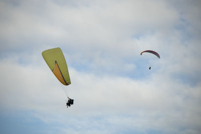 Low angle view of people paragliding against sky