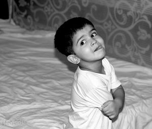 High angle view of boy sticking out tongue sitting on bed at home