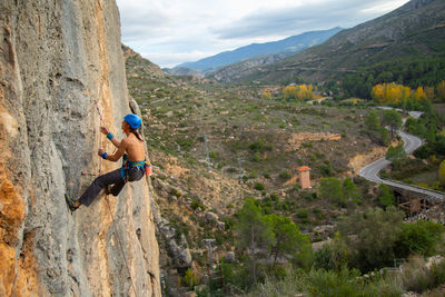 Shirtless man rock climbing against landscape