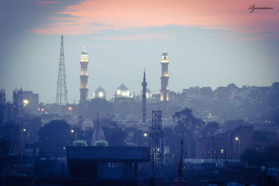 Illuminated buildings in city against sky during sunset