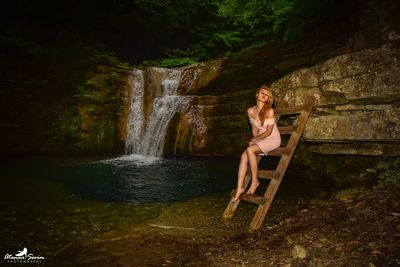 Woman sitting on seat against waterfall