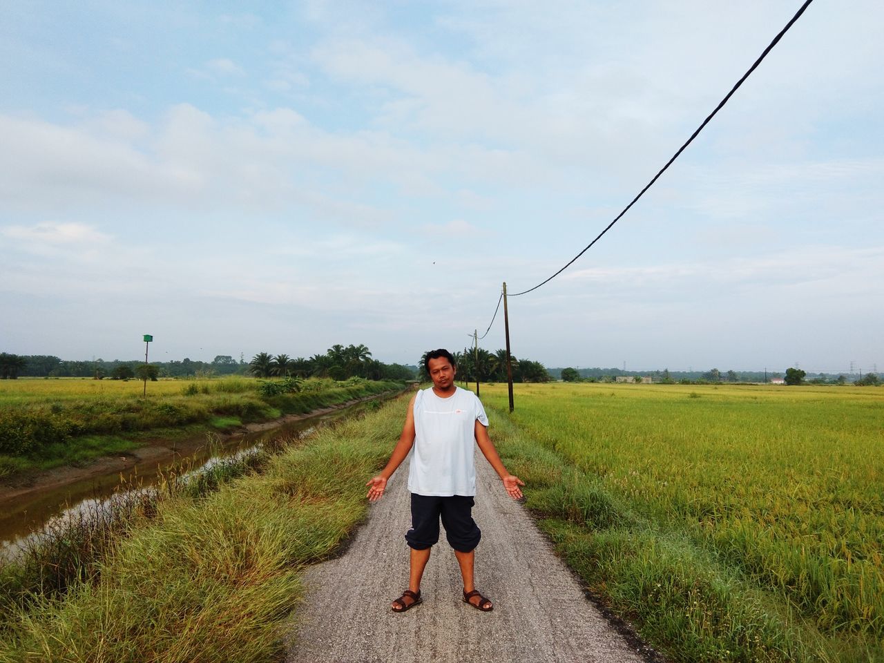 sky, one person, front view, real people, full length, land, field, landscape, cloud - sky, plant, nature, growth, environment, grass, day, casual clothing, standing, lifestyles, leisure activity, diminishing perspective, outdoors