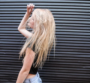 Side view of young woman with tousled blond hair by closed shutter