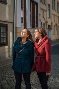 Women standing on footpath against buildings in city