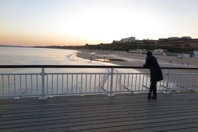 Side view of woman walking on shore against sky during sunset