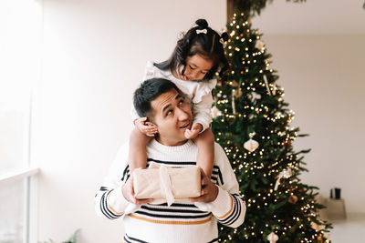 Funny dad and little daughter in sweaters are holding a gift box for the christmas holiday at home