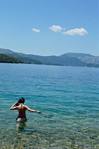 Rear view of woman standing at sea against sky during sunny day