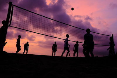 Silhouette people playing volleyball at beach against sky during sunset