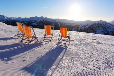 Deck chairs on snow covered mountain against sky