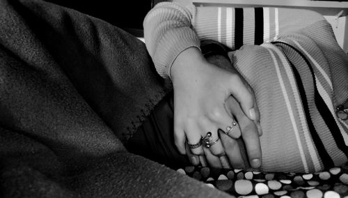 Cropped image of couple holding hands while lying on bed at home