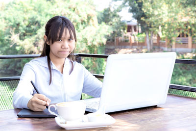 Young woman using mobile phone while sitting on table