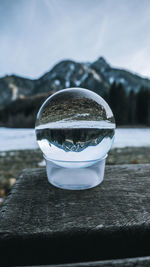 Close-up of crystal ball by calm lake against sky