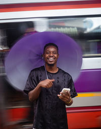 Portrait of man standing in rain holding a mobile phone smiling 