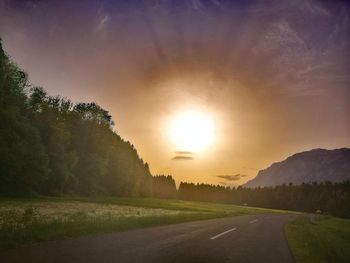 Road by trees against sky during sunset