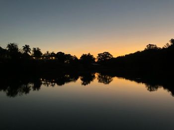 Silhouette trees by lake against sky during sunset