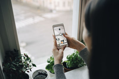 Close-up of girl photographing through smart phone from window