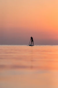 Silhouette person standing on sea against orange sky