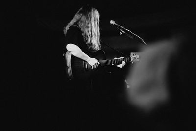 Woman playing guitar against black background