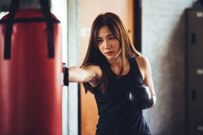 Confident of young woman punching bag while standing in gym