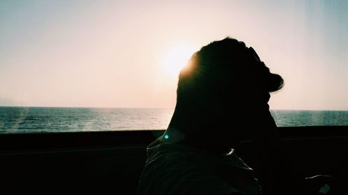 Rear view of silhouette man sitting at beach against sky during sunset