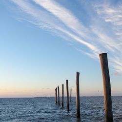 Wooden posts in sea against sky