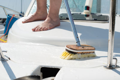 Man washing white boat with brush and pressure water system at pier. yacht maintenance concept.