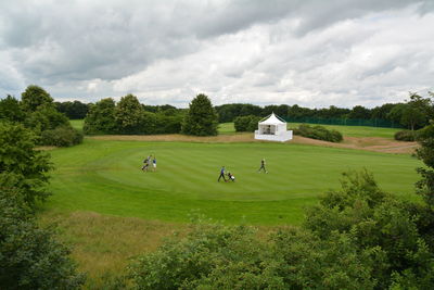 High angle view of men on golf course against cloudy sky