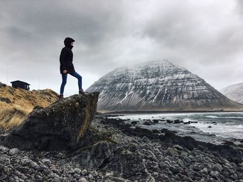 Man standing on rock by sea against sky