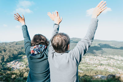 Rear view of woman with arms raised standing against sky