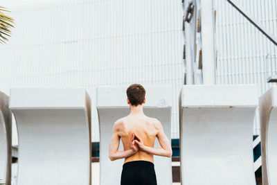 Rear view of shirtless man standing against wall