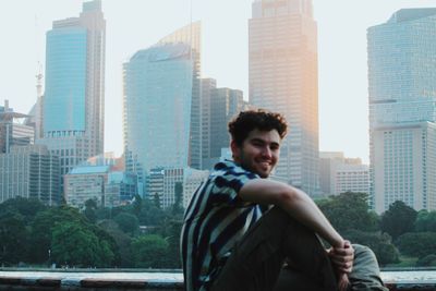 Portrait of young man looking away against buildings in city