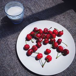 High angle view of cherries in plate by milk glass on table