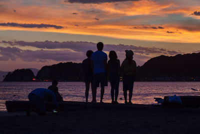 Silhouette people sitting on beach against sky during sunset
