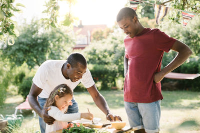 Boy looking at father assisting sister in preparing food at table during garden party