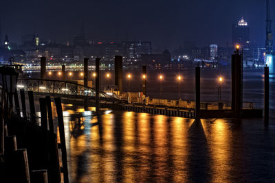 Illuminated bridge over river in city at night