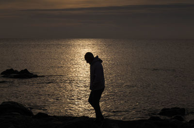 Silhouette woman standing at beach against sky during sunset