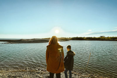 Rear view of woman standing by lake against sky