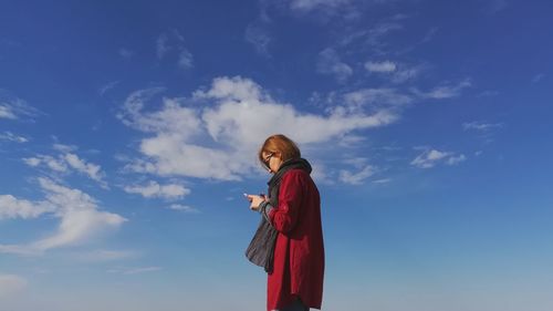 Side view of woman using mobile phone while standing against blue sky