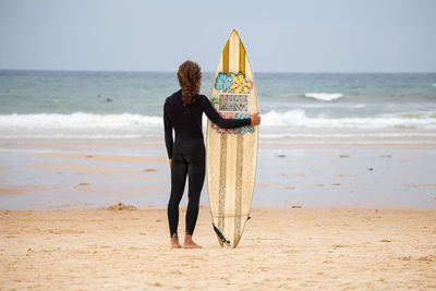 Rear view of man standing with surfboard at beach