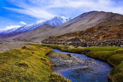 Scenic view of stream by mountains against sky