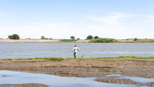 Rear view of man standing and fishing at beach against sky